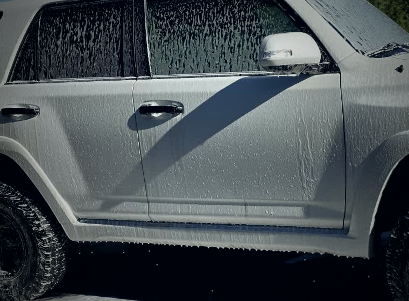 Snow foam clinging to the flank of a white 4Runner mid-wash